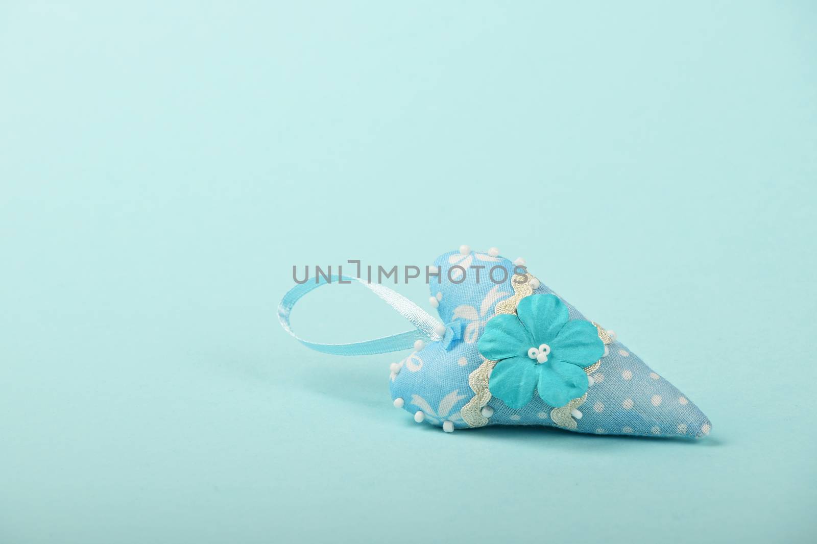 One small textile heart with mulberry paper flower and ribbon on tender blue background