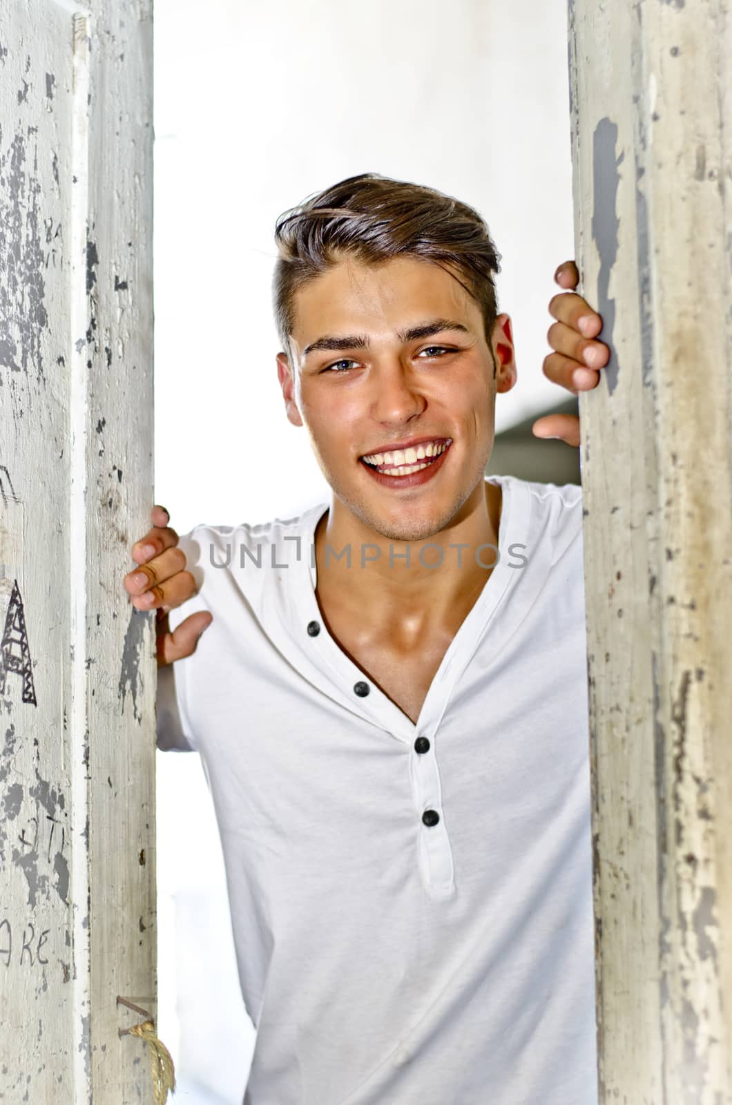 Handsome smiling young man opening old door, inviting viewer to enter