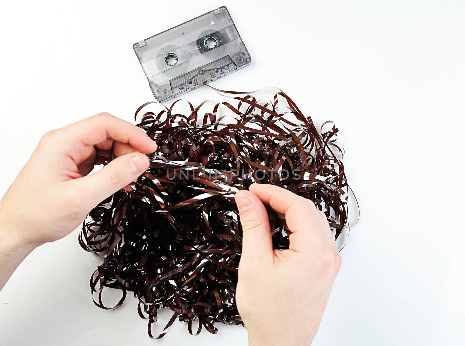 hands uncurving audio tape on white background