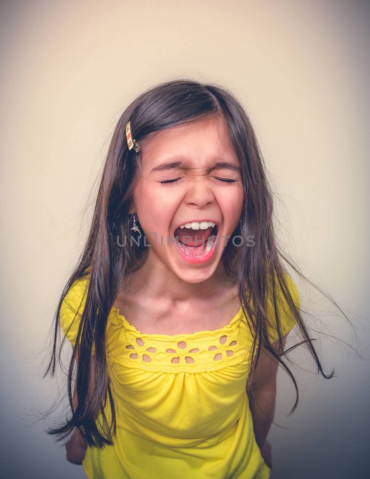 A young girls screams at the top of her lungs while her eyes are closed.