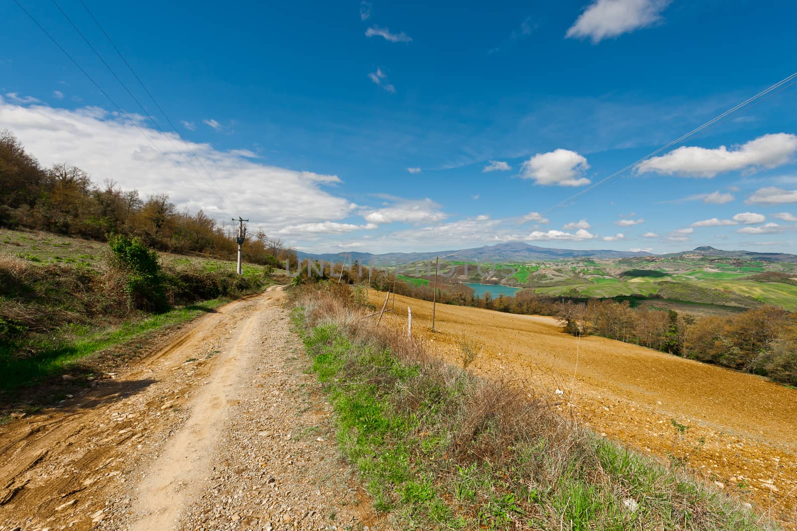 The Dirt Road Leading to the Mountain Lake Surrounded by Forests and Plowed Fields in Italy
