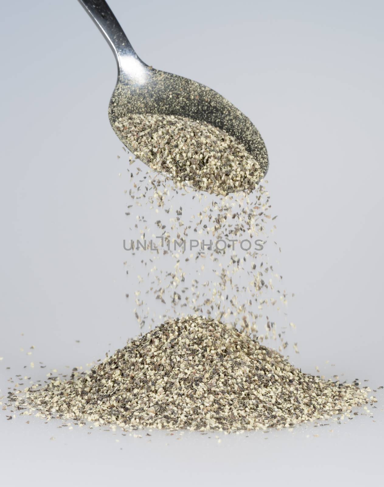 Black Pepper Falling from tablespoon close up.
