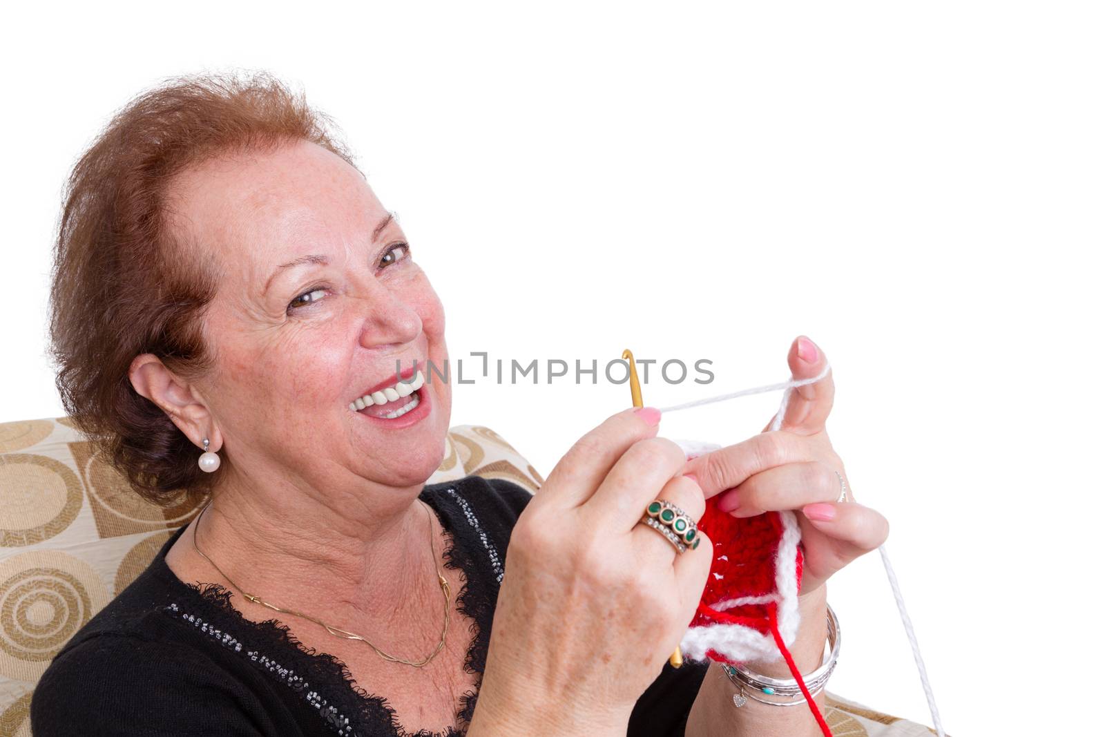 Laughing elegant senior lady sitting knitting a colorful red item as she enjoys her retirement, close up head and shoulders over white with copyspace