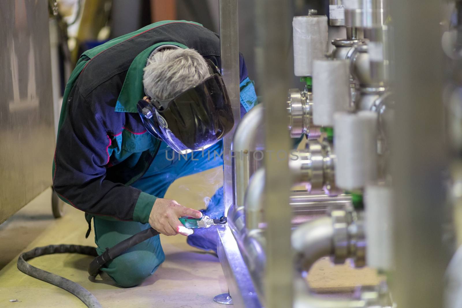 Industrial worker with protective mask welding inox elements in steel structures manufacture workshop.