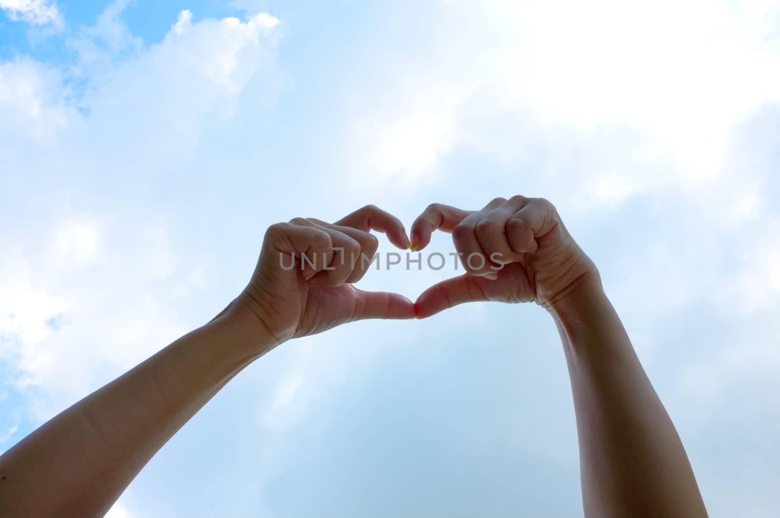 Hands shape of heart beneath blue sky