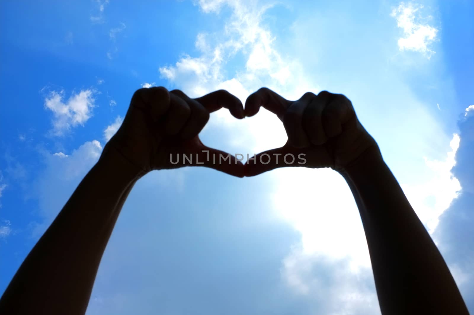 Hands shape of heart beneath blue sky