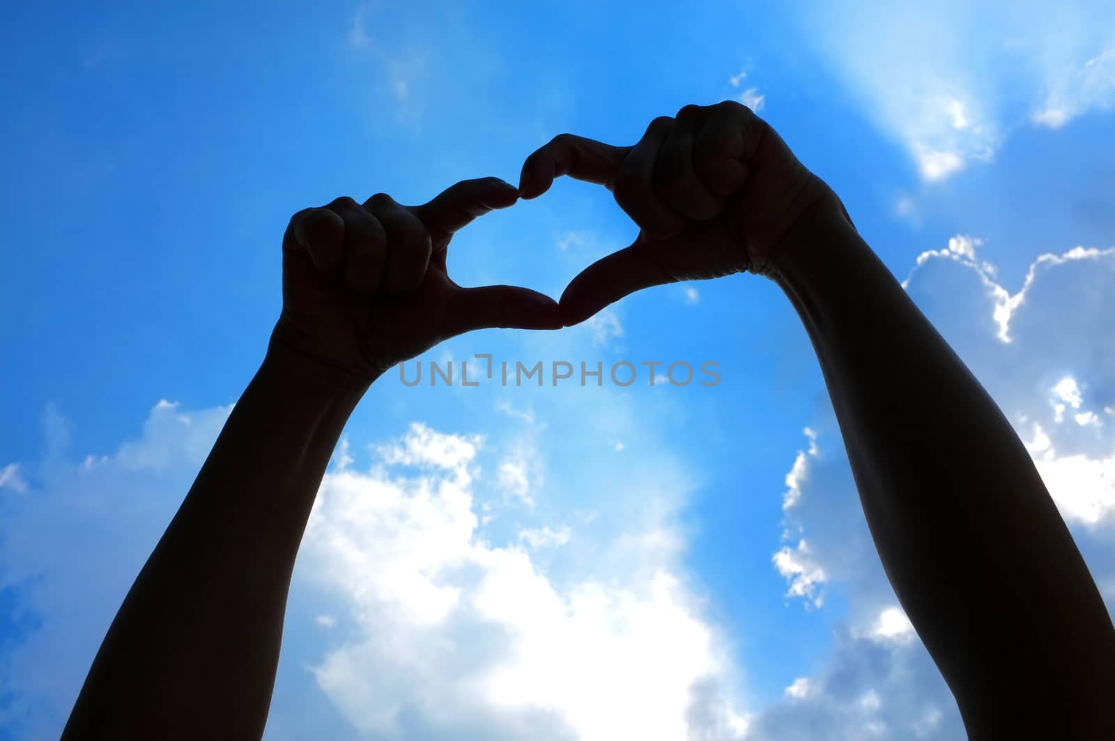 Hands shape of heart beneath blue sky