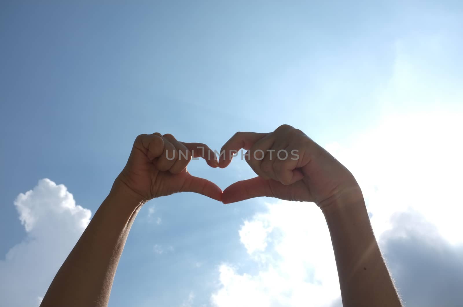 Hands shape of heart beneath blue sky