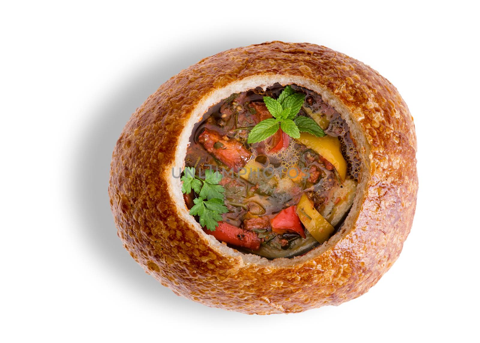 Wholesome vegetable soup with eggplant, brinjal or aubergine, in a sourdough bread bowl garnished with fresh parsely and mint viewed from above over a white background