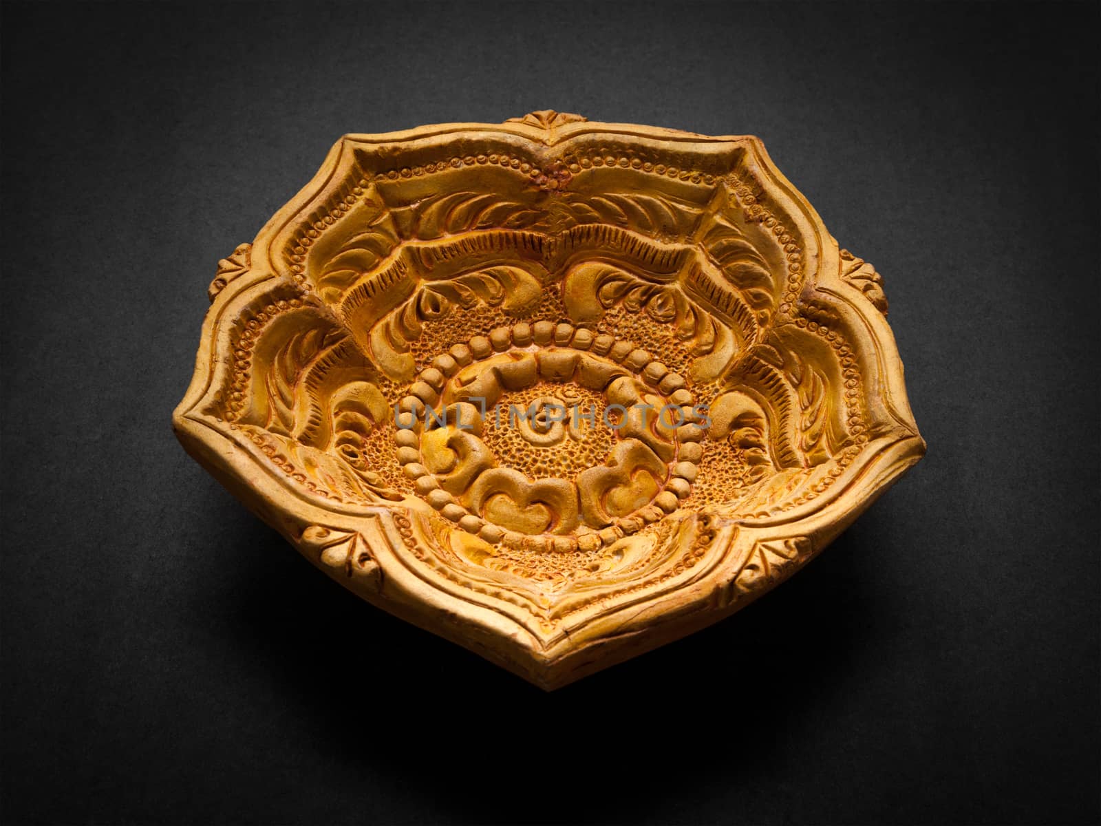 Front view of a beautifully carved designer handmade clay lamp on dark background.