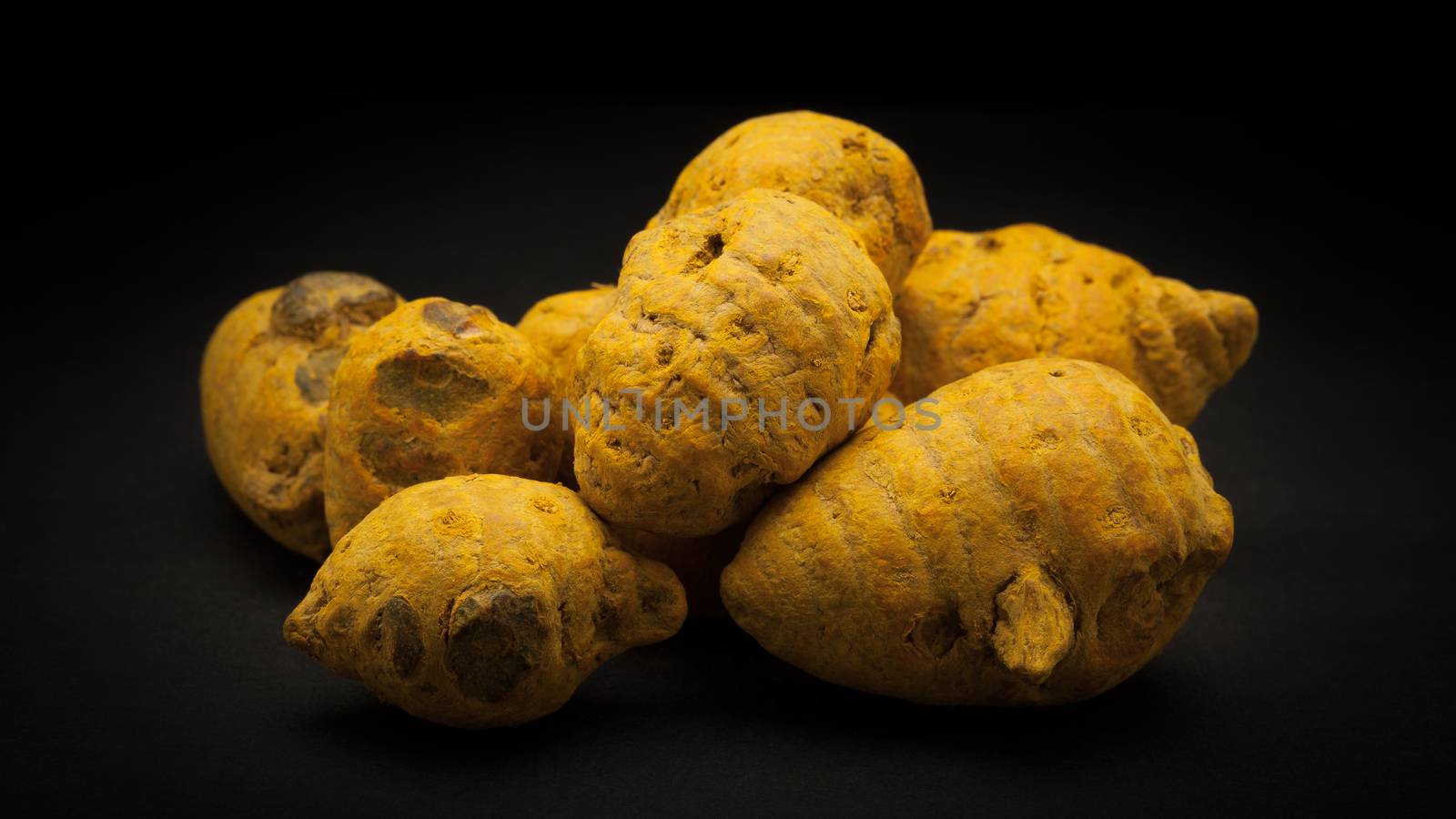 Pile of Organic Round Turmeric or Haldi (Curcuma longa) on dark background.