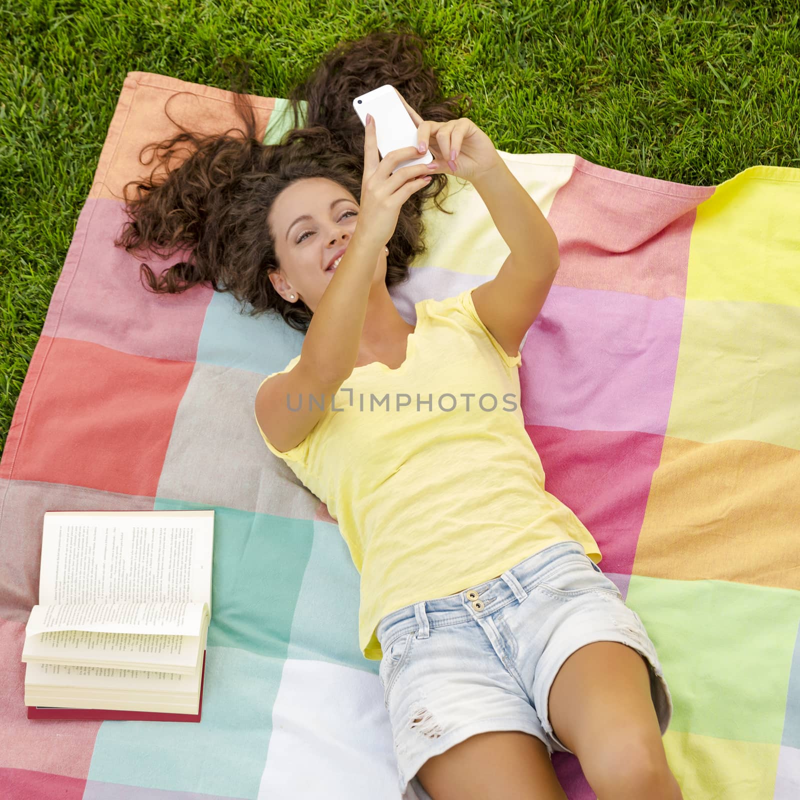 Smiling young woman lying on a blanket and making a selfie