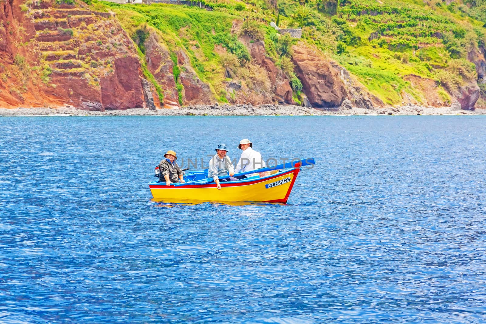 Calheta, Madeira - June 8, 2013: Three friendly fishermen on yellow motorboat offshore of Calheta in the west of Madeira island.