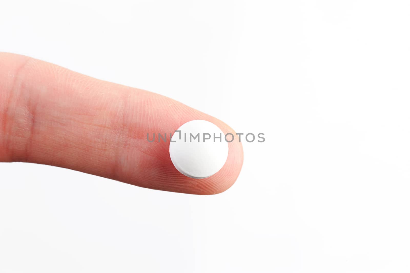 white round pill lay on finger on white background