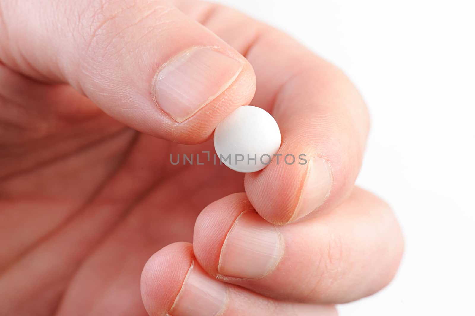 macro of white round pill in hand on white