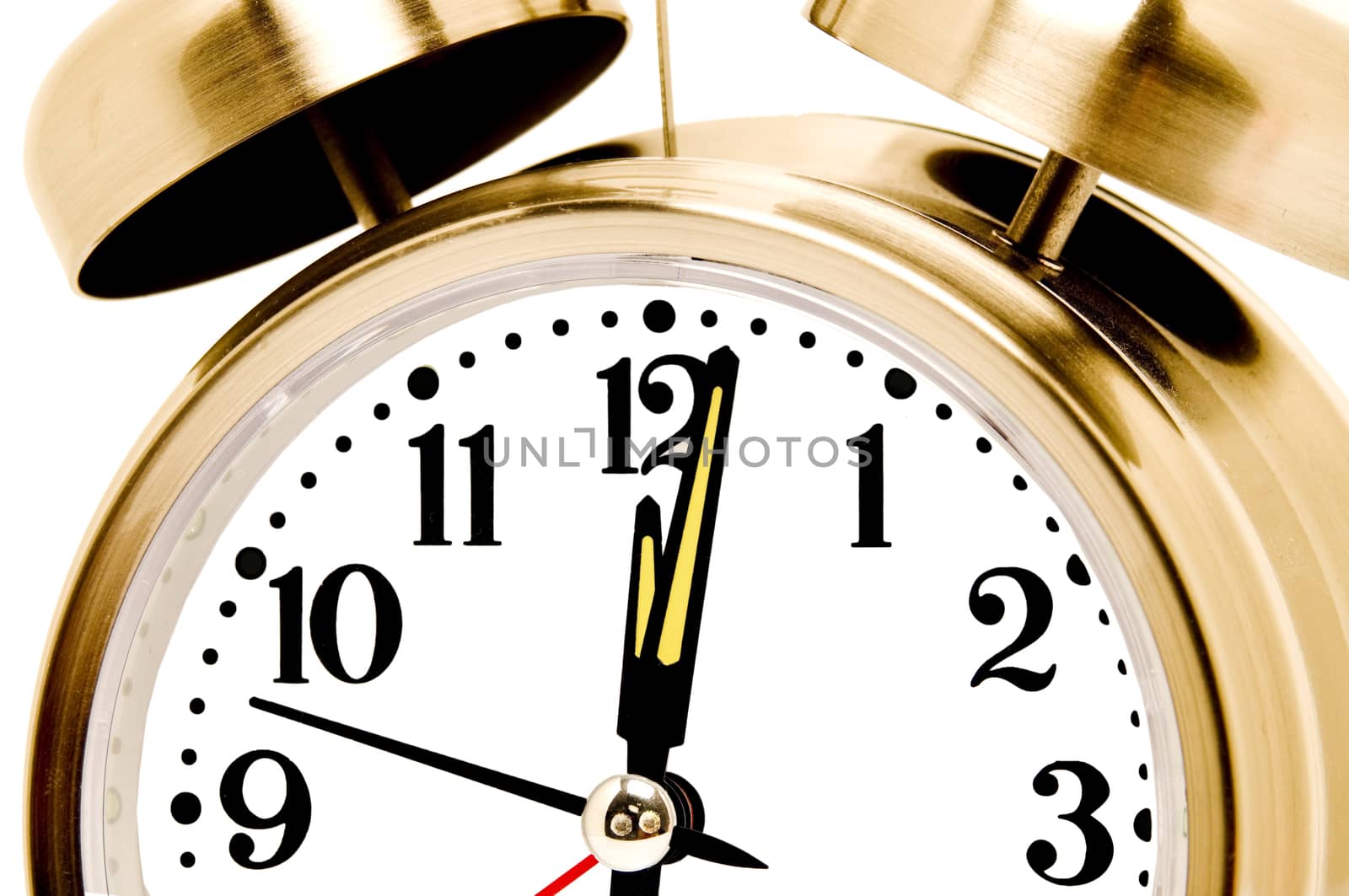 Horizontal close up shot of a vintage brass alarm clock with glow in the dark hands on white background.