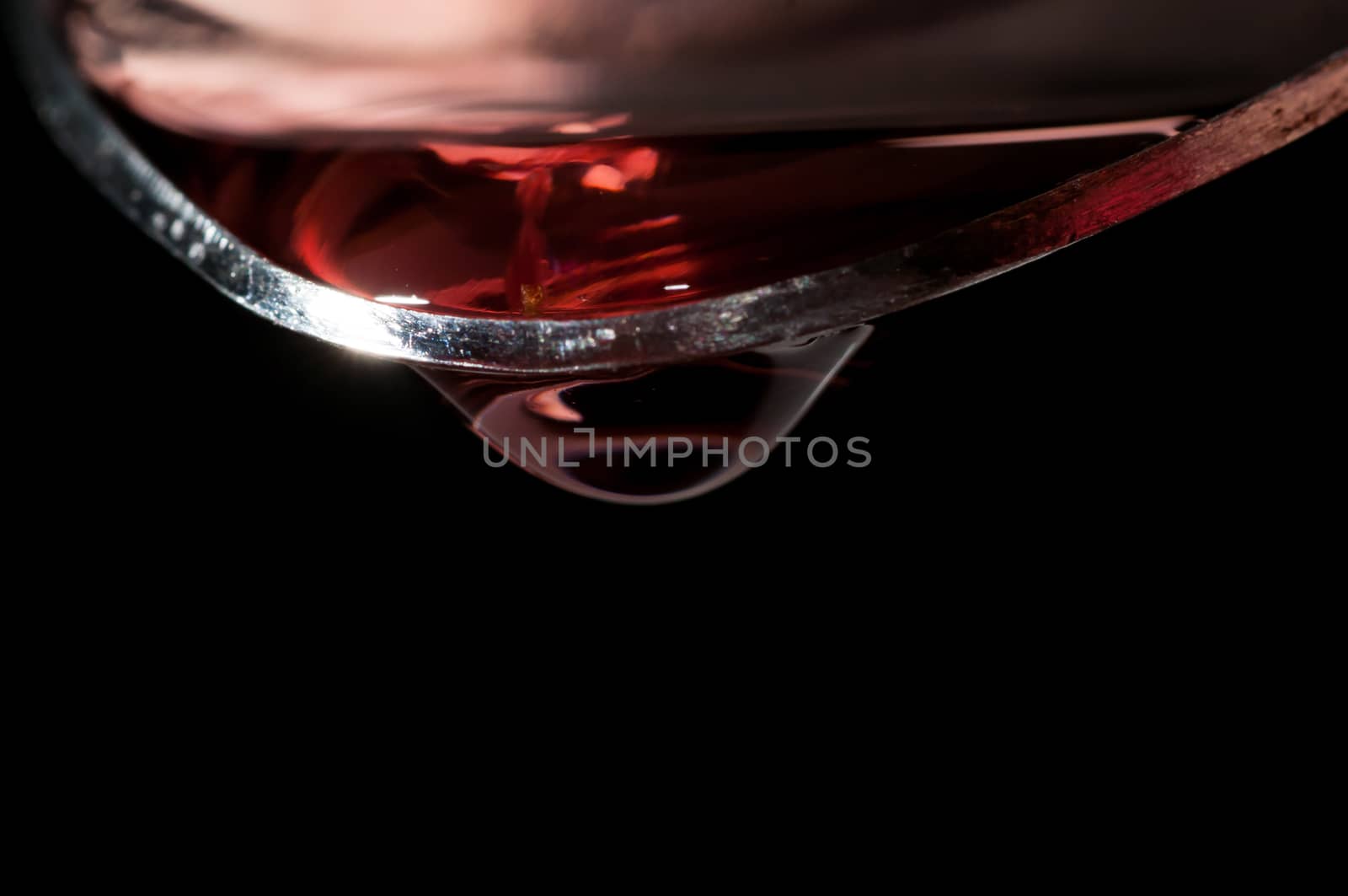 Droplet of Red medicine falling from a large silver spoon