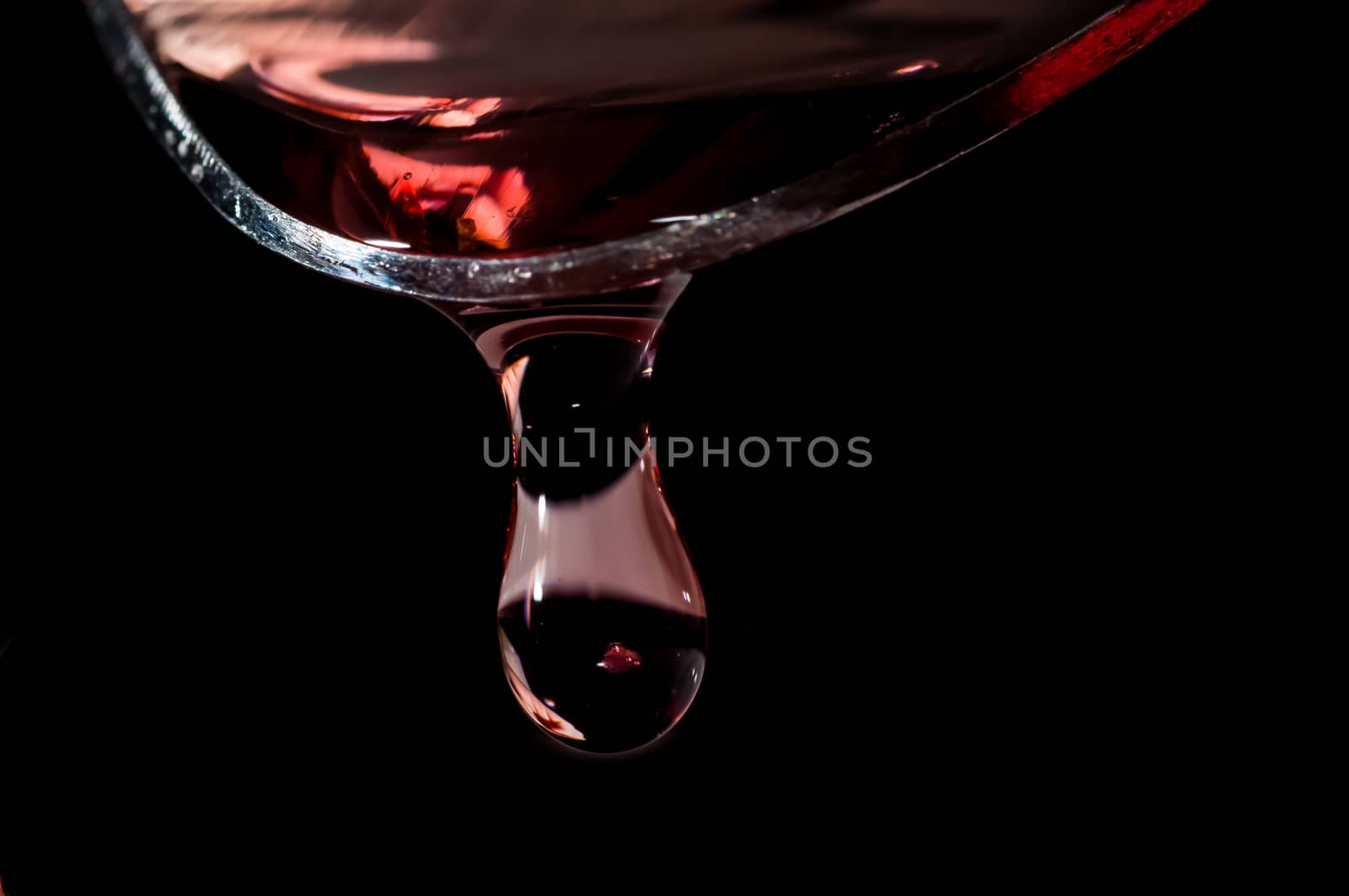 Droplet of Red medicine falling from a large silver spoon