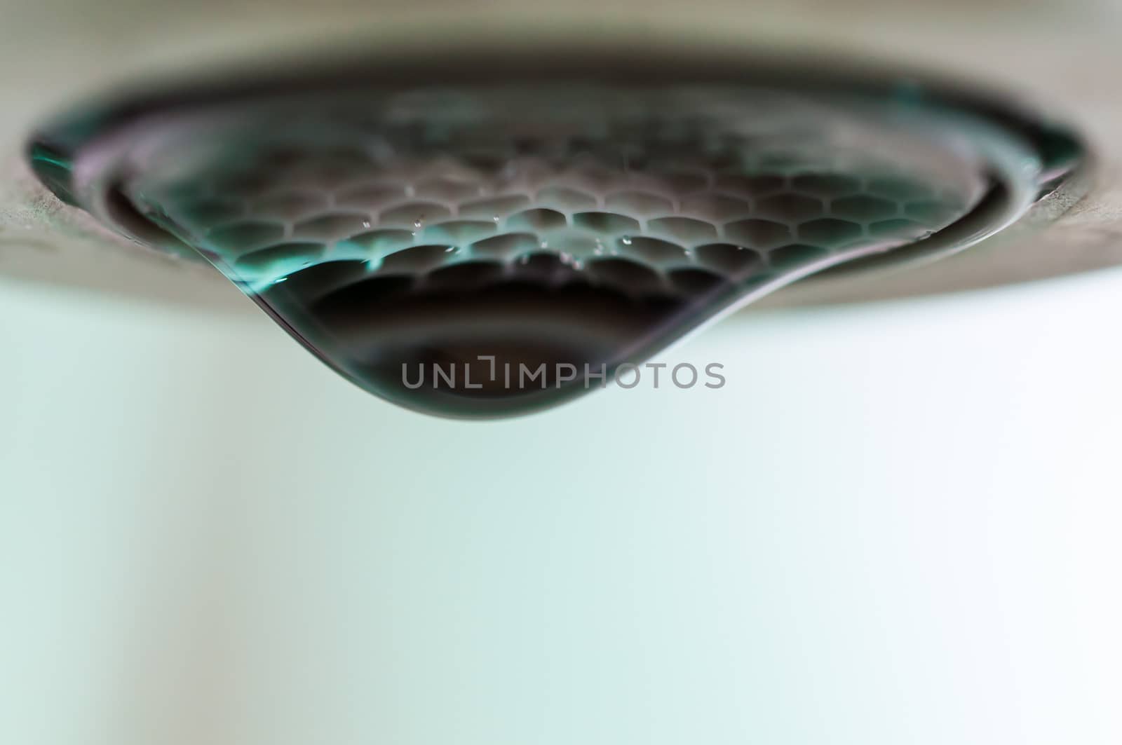Droplet of water about to fall from a green tinted faucet