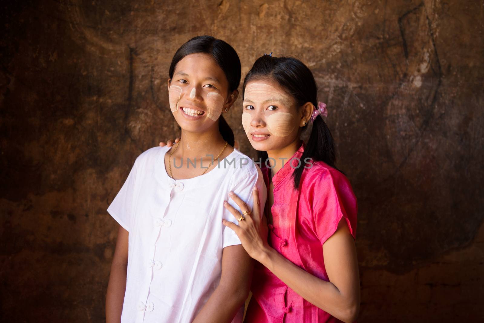 Portrait of two pretty Myanmar girls smiling, low light inside a temple.