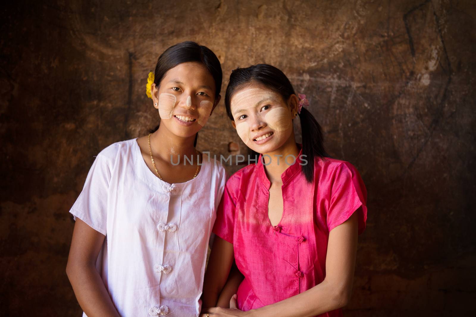 Portrait of two beautiful Myanmar girls smiling, low light inside a temple.