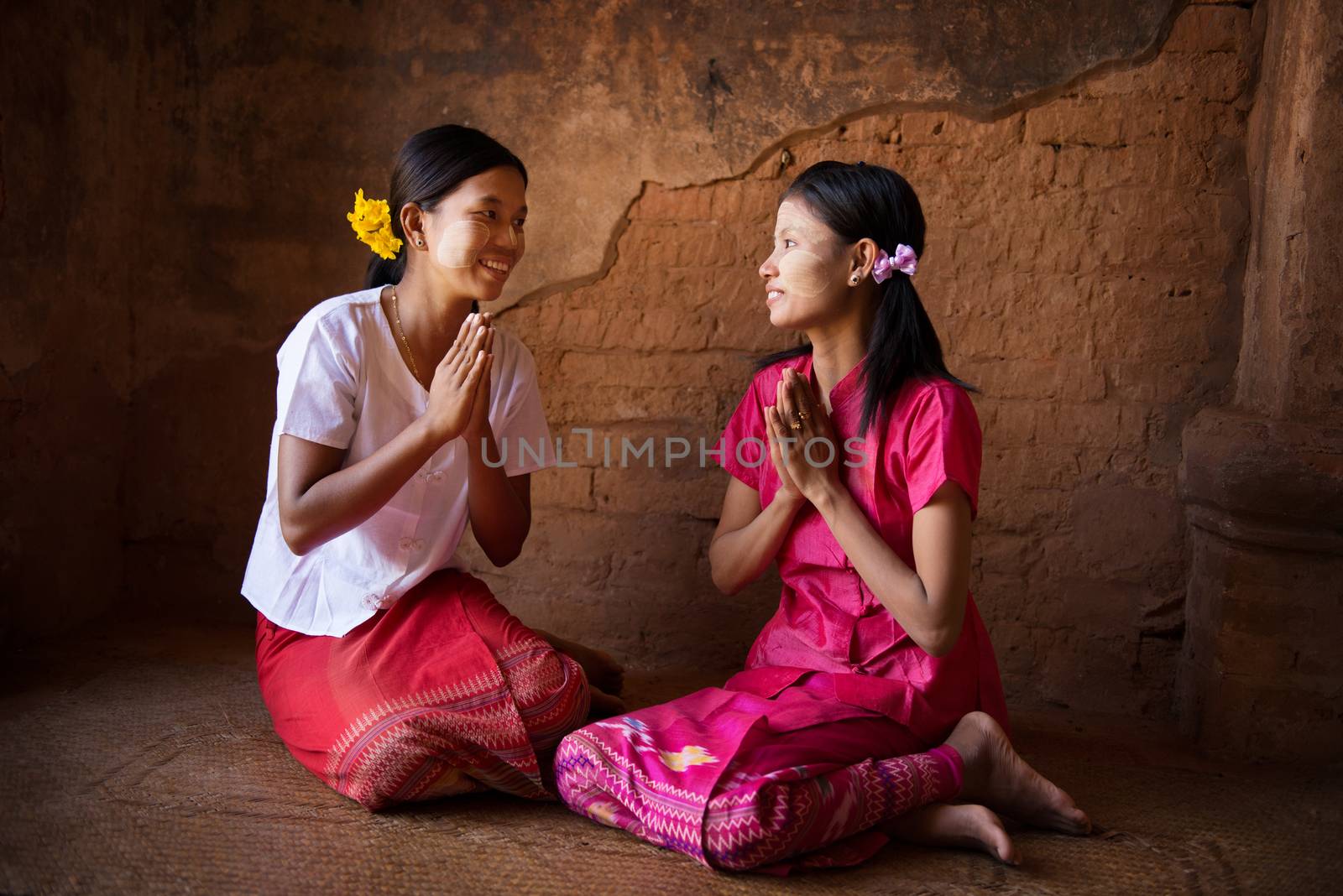 Two young Myanmar girl in a traditional welcoming gesture, sitting inside temple.