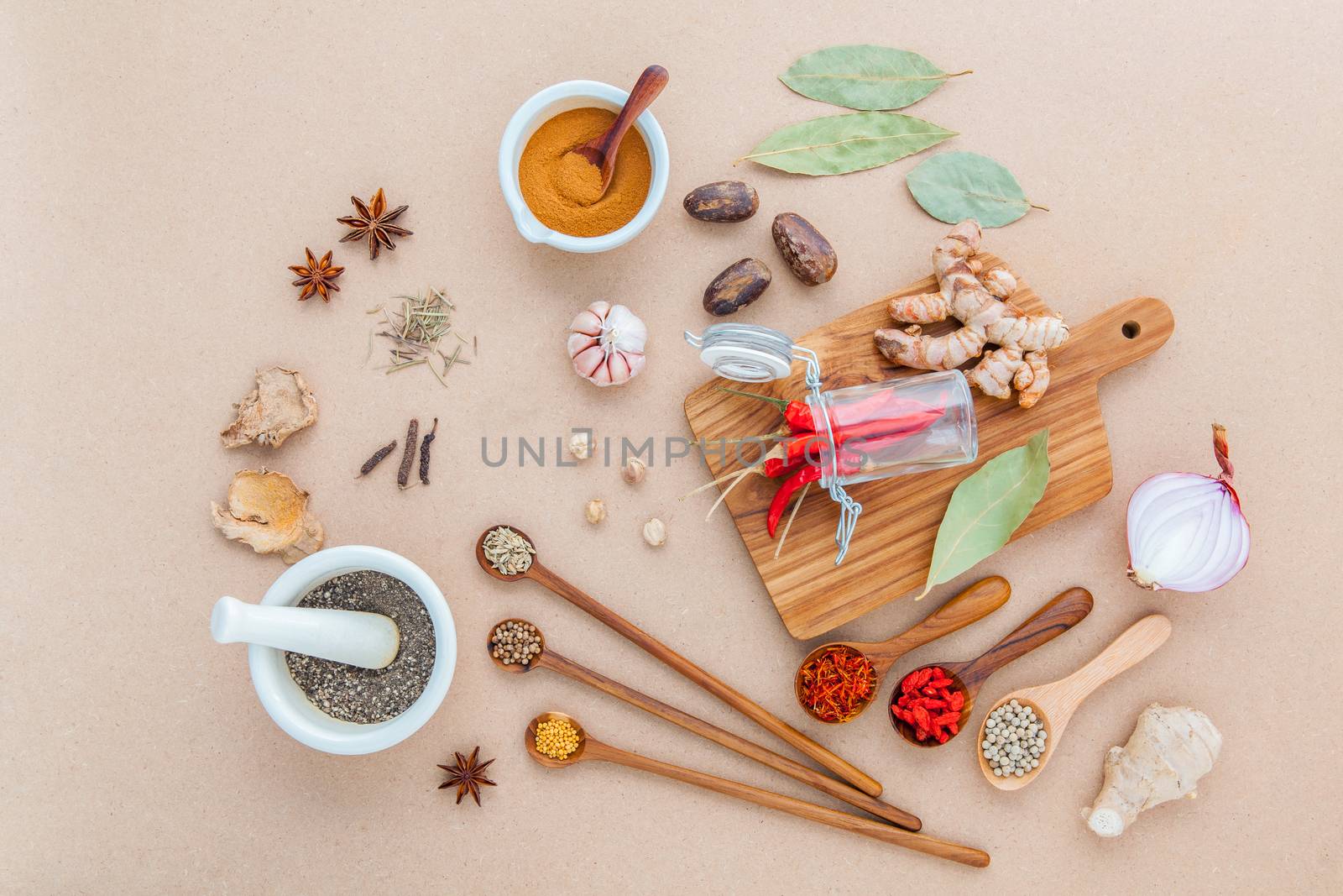 Composition of Mixed spices and herbs background cinnamon stick and cinnamon powder in white mortar with star anise ,bay leaves,onion ,ginger,galangal,saffron ,rosemary and wooden spoon on brown background .