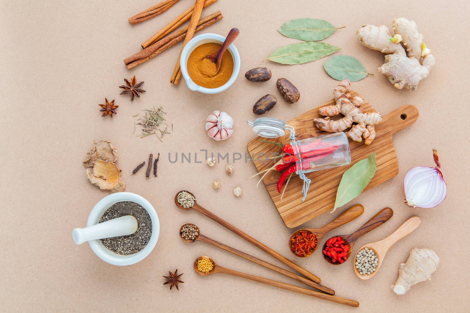 Composition of Mixed spices and herbs background cinnamon stick and cinnamon powder in white mortar with star anise ,bay leaves,onion ,ginger,galangal,saffron ,rosemary and wooden spoon on brown background .