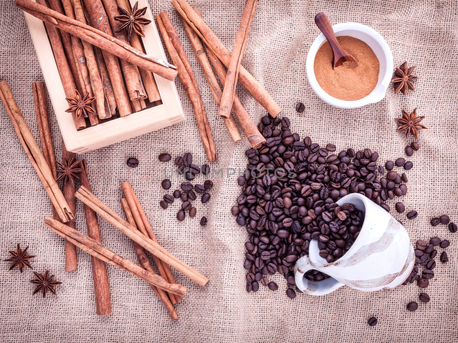 The Cup of coffee beans on the cloth sack with cinnamon sticks ,cinnamon powder in the bowl and star anise.