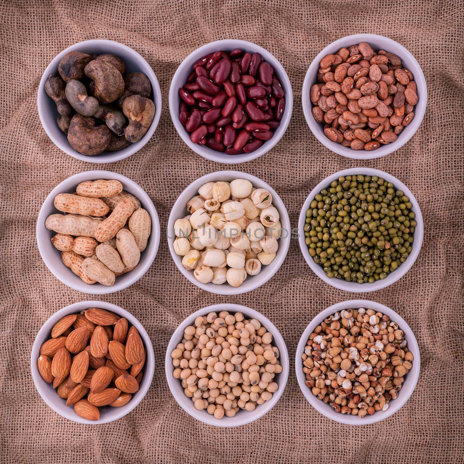 Mixed beans , lentils and nuts in the white bowl on brown cloth sack  background. mung bean, groundnut, soybean, red kidney bean , lotus seed ,almond,green bean,millet,cashew and brown pinto beans .