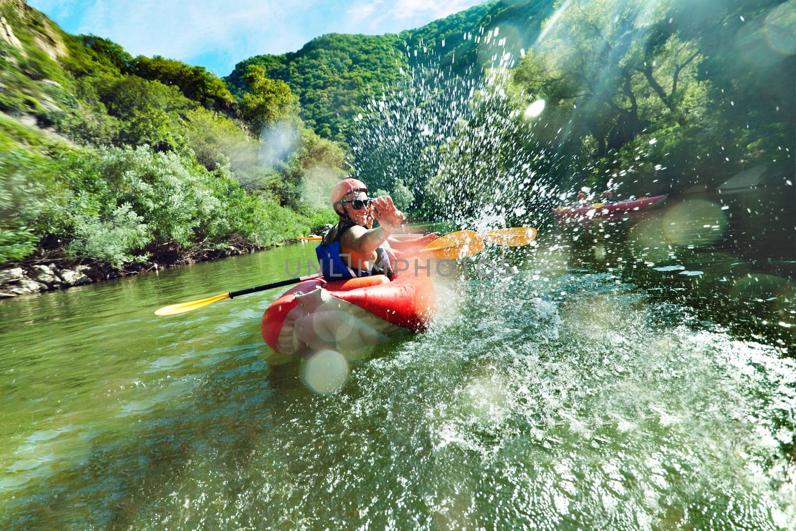 A male is looking back at camera and splahsing in red inflatable canoe having fun in calm waters of a river.