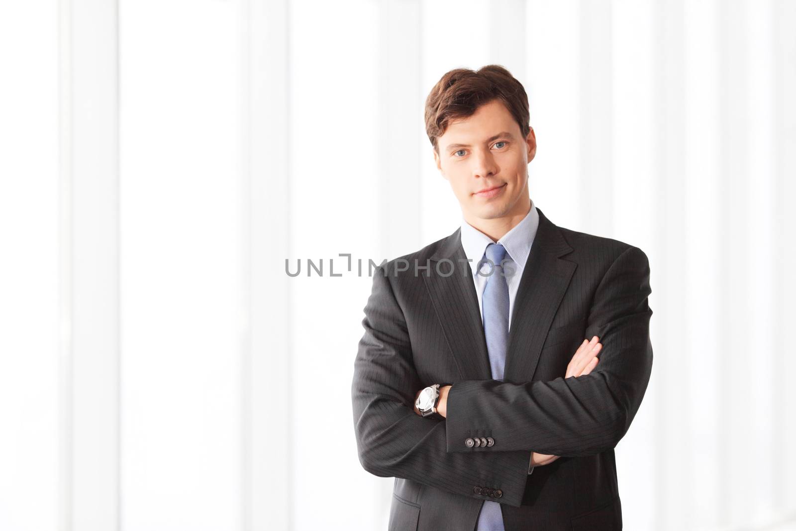 Portrait of handsome businessman standing near windows in office