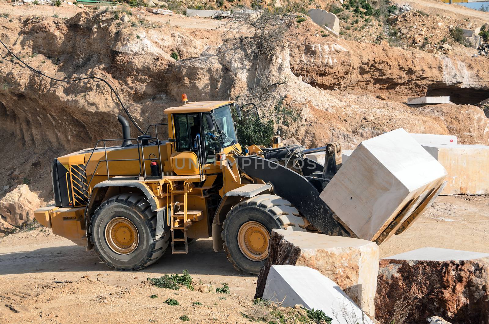 Industrial marble quarry, with cut blocks and workers and machines bulldozer at work.