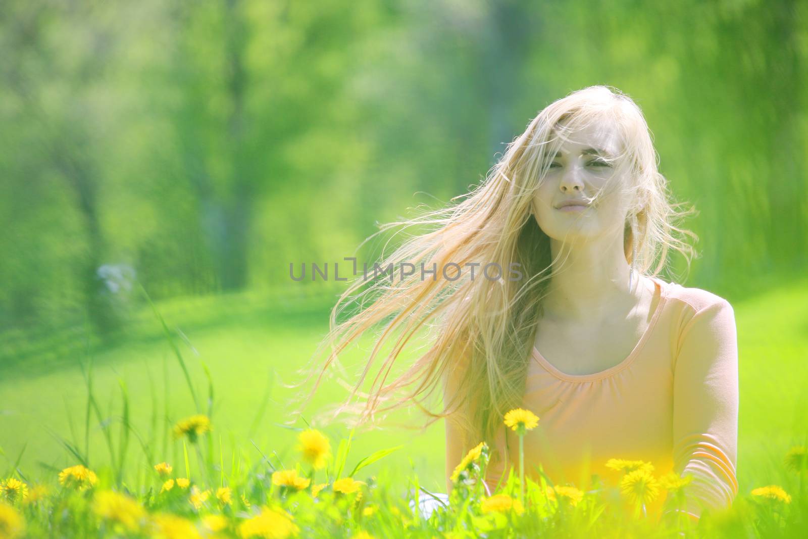 Beautiful young woman laying in spring park with dandelion flowers