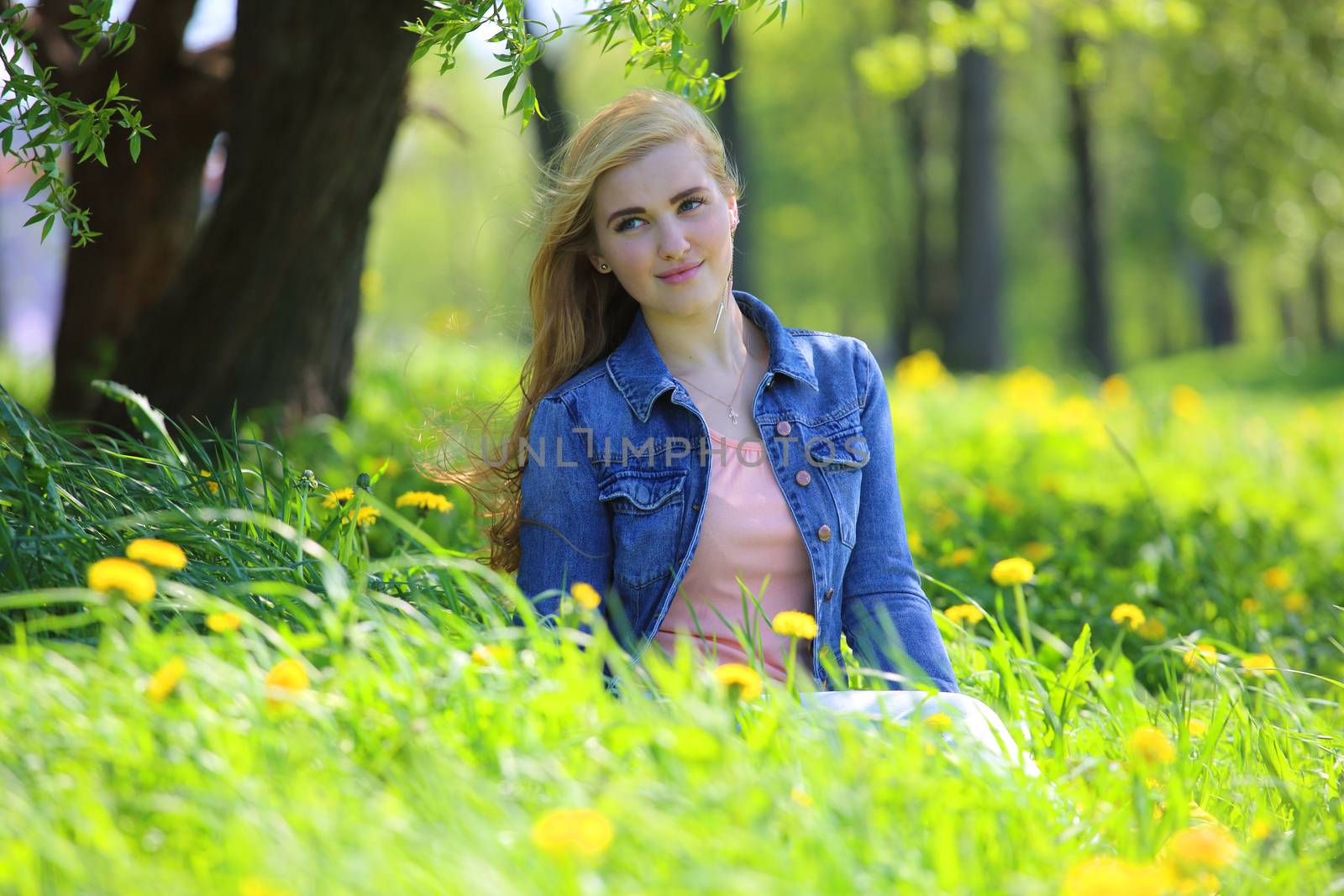 Beautiful young woman sitting in spring park with dandelion flowers