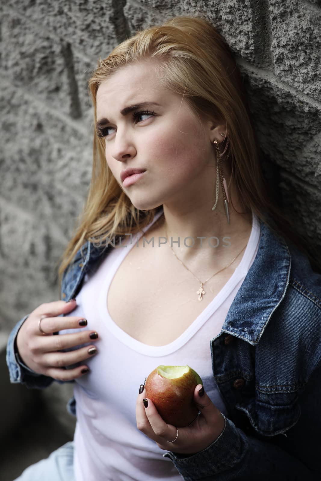 Urban style portrait of young beautiful blond woman in denim with apple