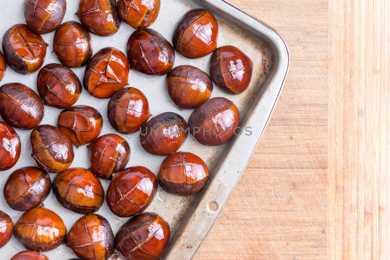 Top view of buttered chestnuts on metal tray ready for baking on wooden table