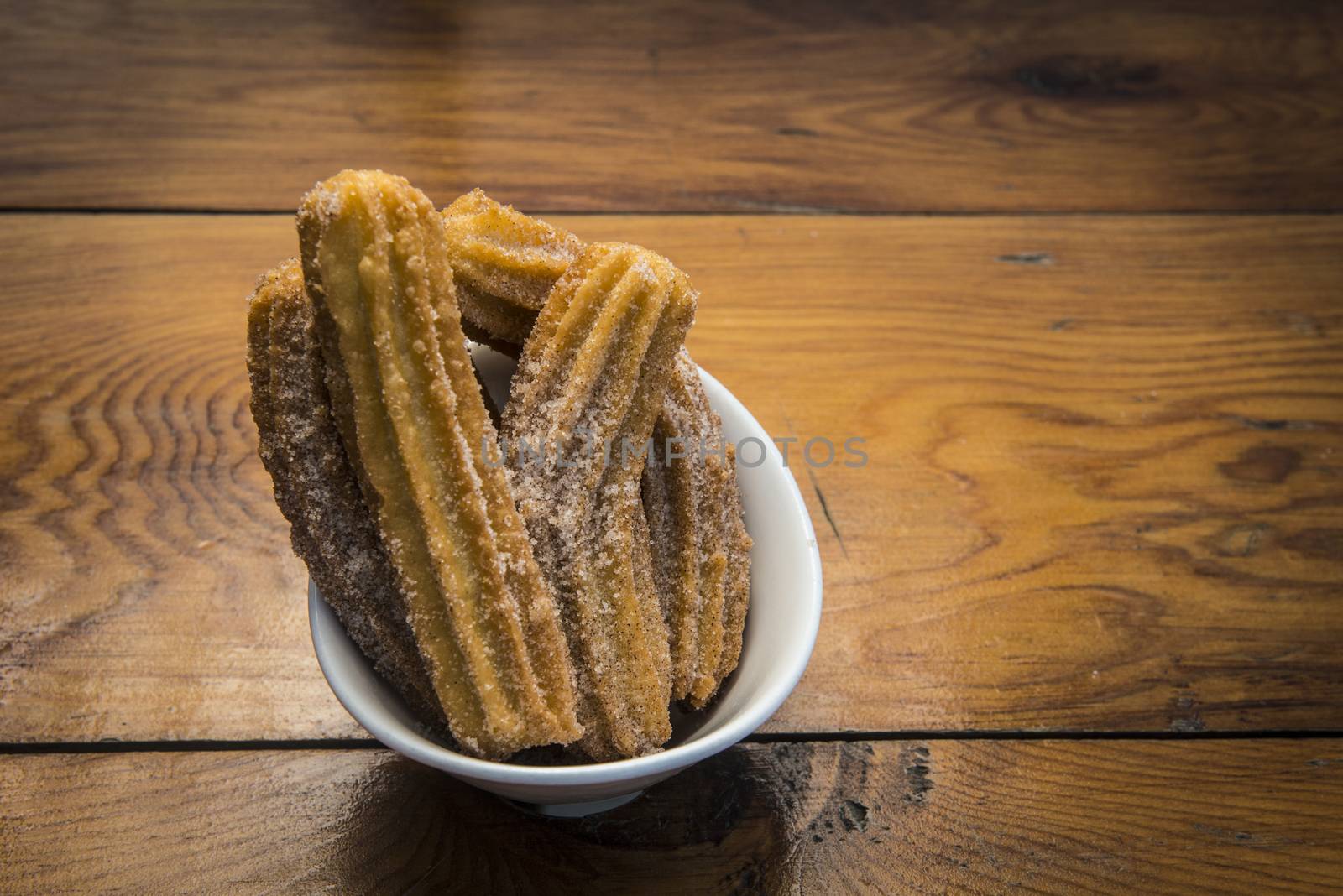 Image of a bowl of fresh churros in a bowl on a wood table