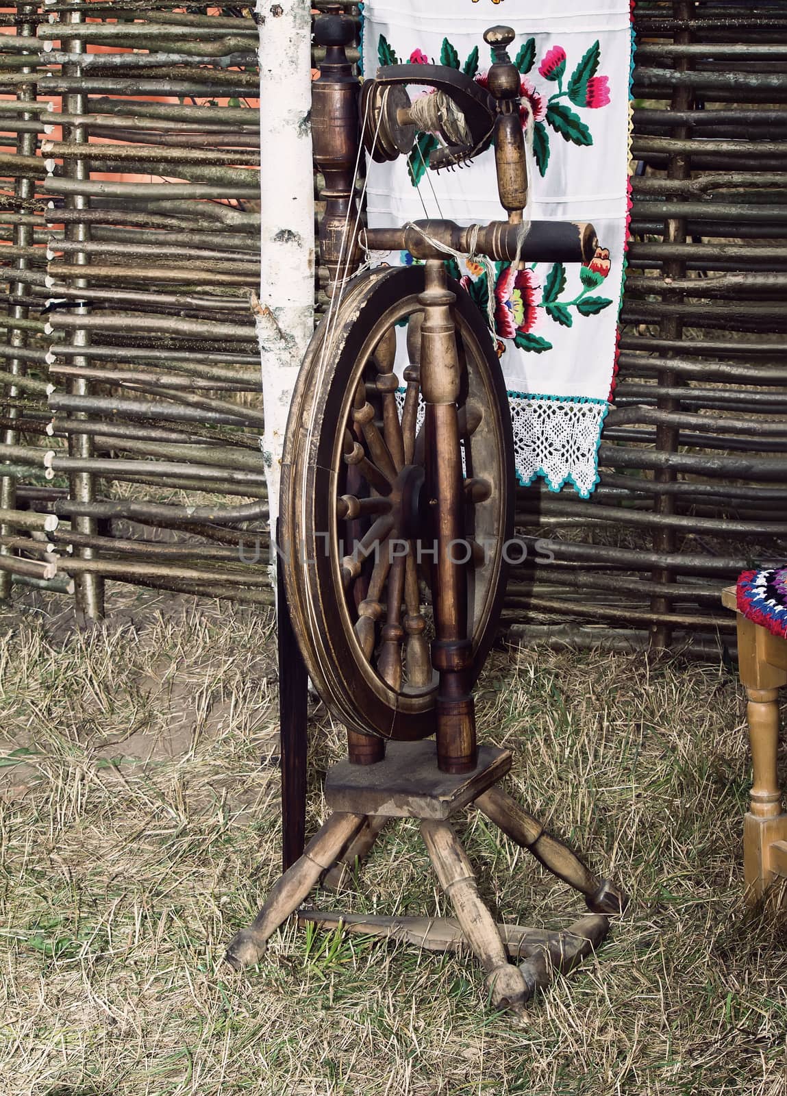 Antique wooden spinning wheel on a background of woven fence. On the fence hangs a beautiful embroidered pattern towel.