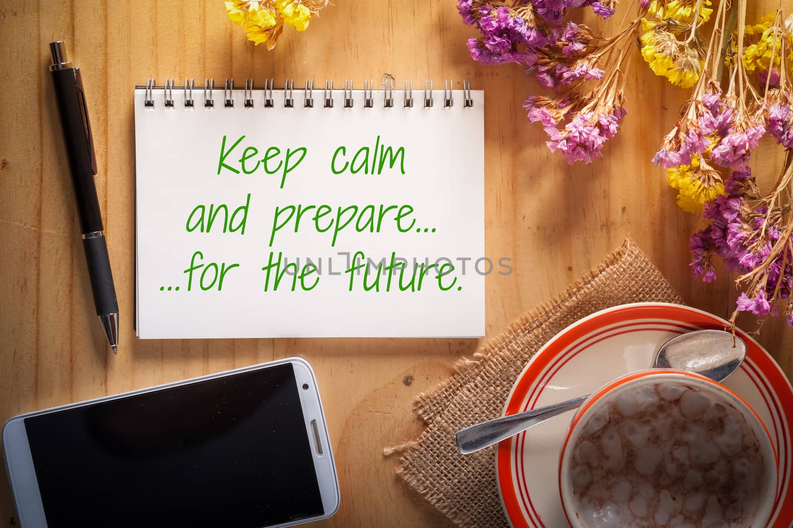 "Keep calm and prepare for the future" is written on notepad with pen, smart phone, and a cup of hot coffee on wood table in afternoon time
