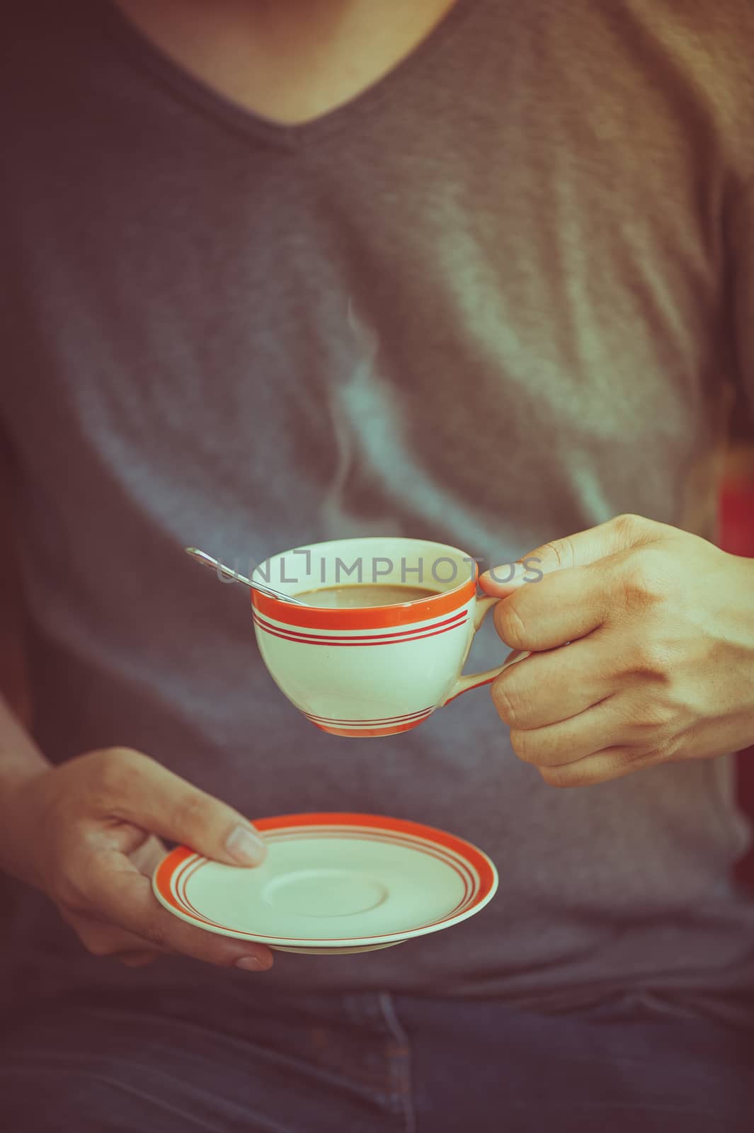 The man wearing grey t-shirt holding coffee cup in his hand in afternoon time with film filter effect