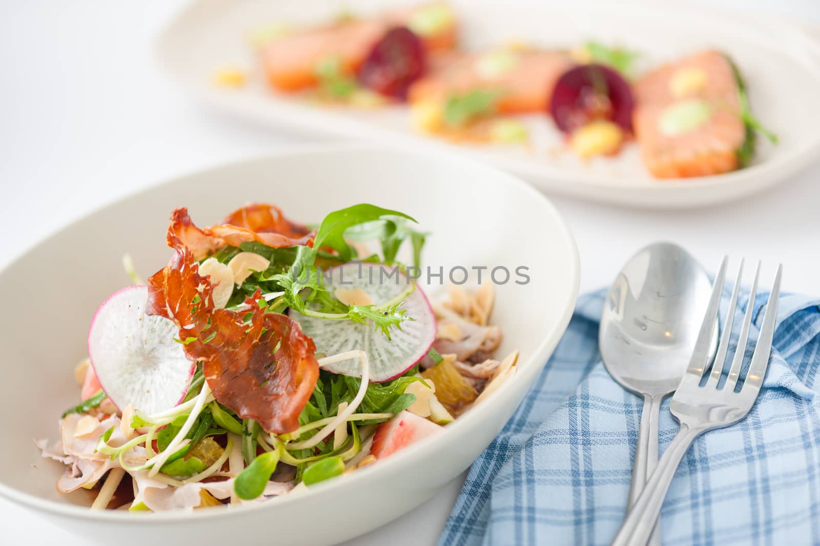 Vegetables and fruits salad with balsamic vinegar and navel orange dressing and smoked striploin ham 1.5 millimeters thickness in ceramic bowl, a modern cusine concept food with another dish of appetizer in background