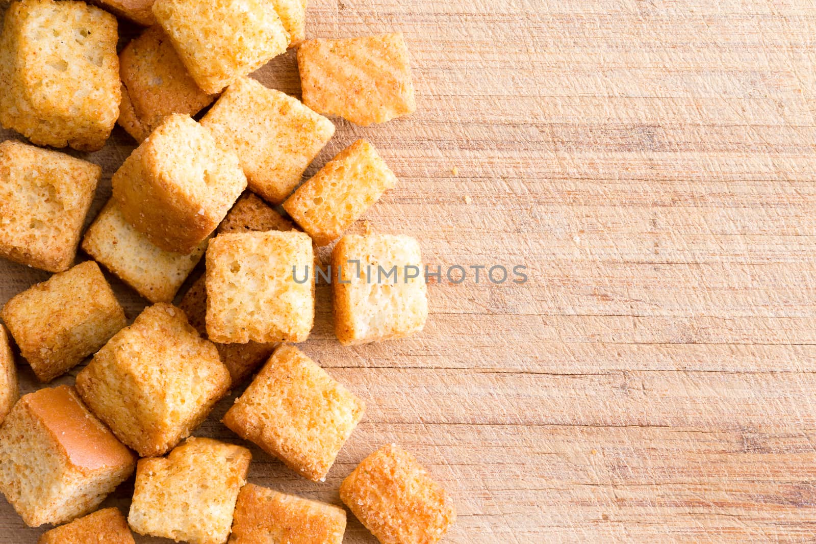Crispy golden freshly sauteed croutons made of cubed white bread as a delicious crunchy addition to a bowl of hot winter soup, overhead on wood with copy space