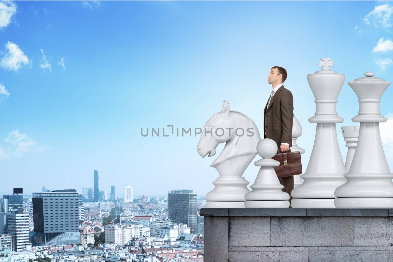 Businessman standing with big chess figures on building roof