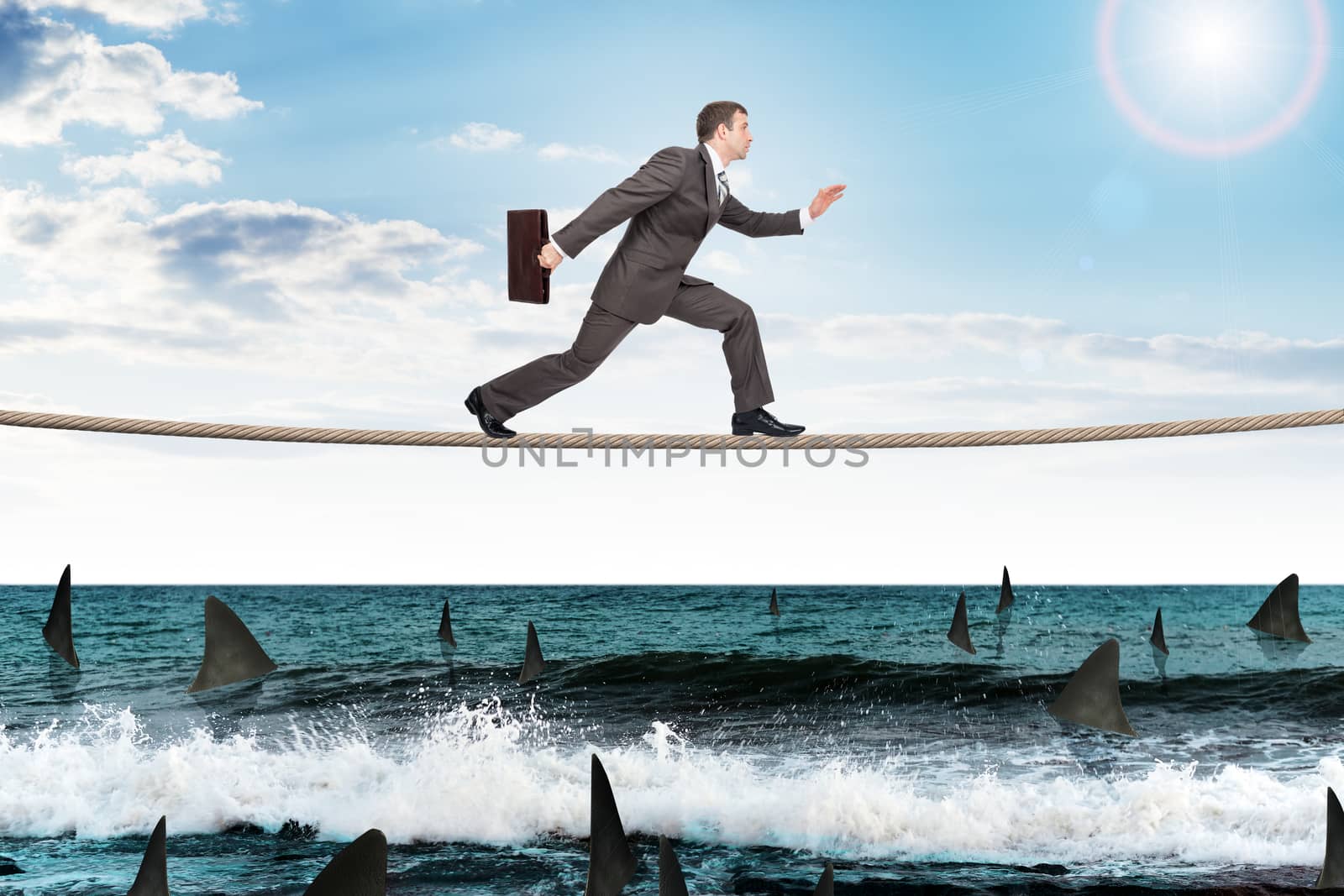 Businessman running on rope above ocean with sharks