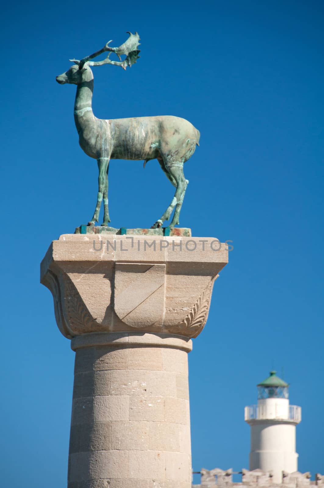 Rhodian deer statue with St Nicholas lighthouse behind. Build on the site of the legendary Colossus of Rhodes the statues guard the harbour to Mandraki Harbour on the greek island of Rhodes.