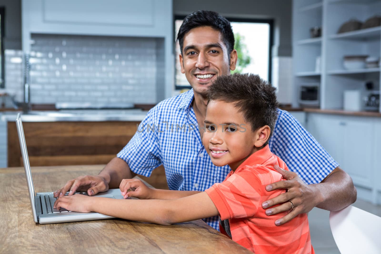 Smiling father using laptop with his son in the kitchen