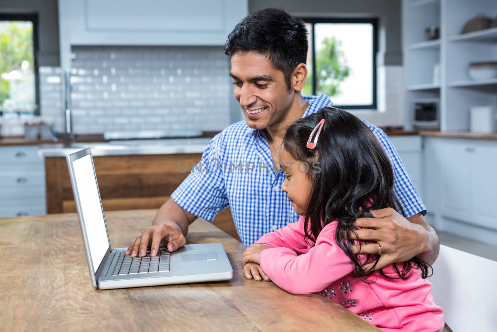 Smiling father using laptop with his daughter in the kitchen