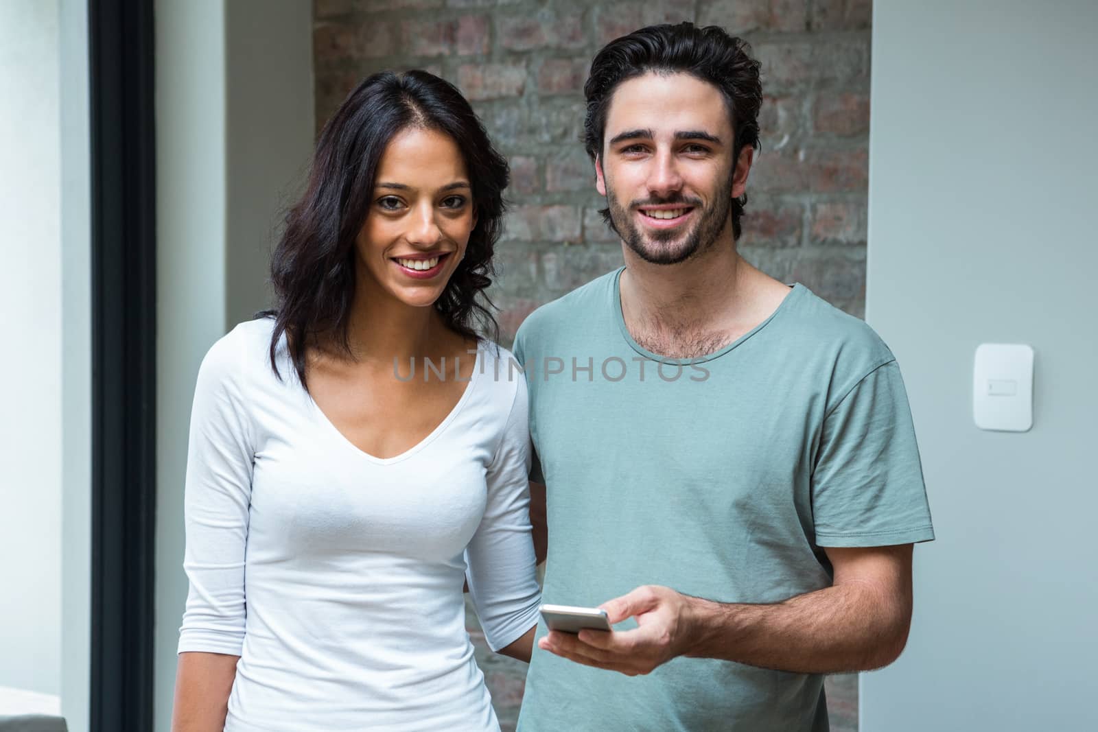 Happy couple using smartphone in living room and looking at the camera