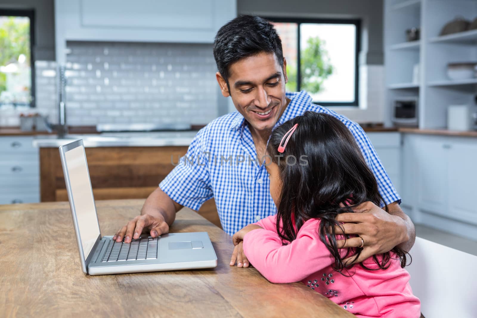 Smiling father using laptop with his daughter in the kitchen